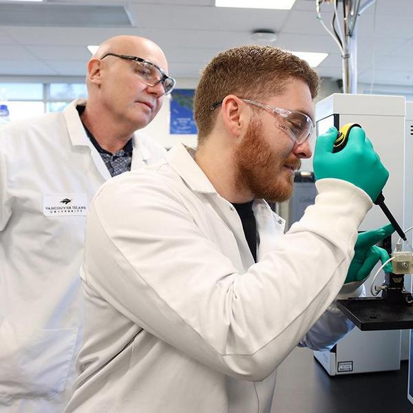 A person holds a dropper over a paper spray sample while a second person looks on