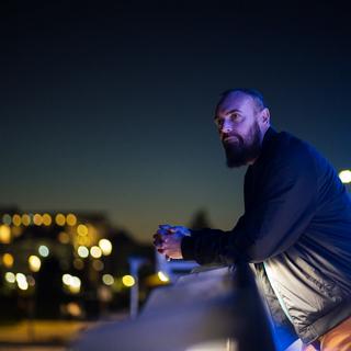 Shanon Sinn leans on a balcony railing and gazes at a night city scape