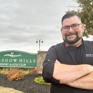 Aaron Smith standing by the Glasgow Hills resort sign with his arms folded and smiling at the camera.