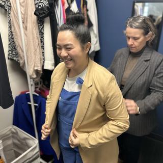 One woman helps another try on a blazer