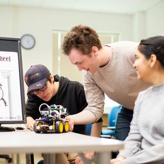 three students look at a robotic car on a table