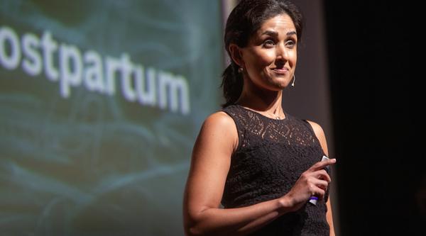 Dr. Shahana speaks on the stage with a clicker in her hand, wearing a mic set