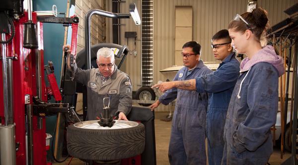three automotive students receive instruction from a teacher in the shop