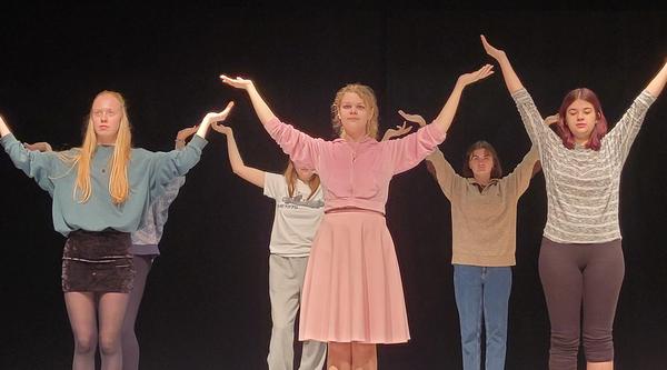 Six actors stand in two lines holding their arms up over their heads while rehearsing a scene at Malaspina Theatre.