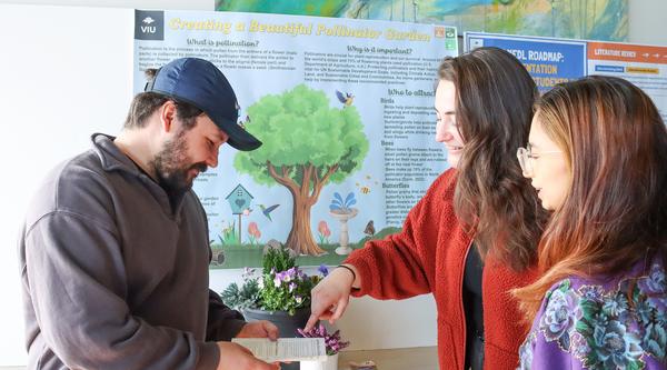 Three students look at a pamphlet in front of their CREATE research poster.