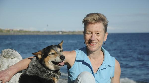 Debra Hellbach sits on the beach with a dog.