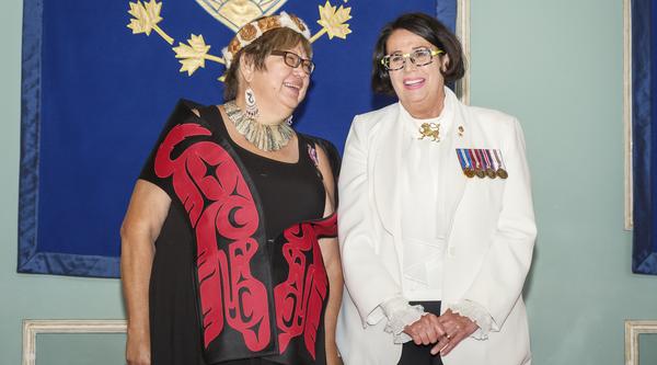 Two people pose in front of the BC coat of arms