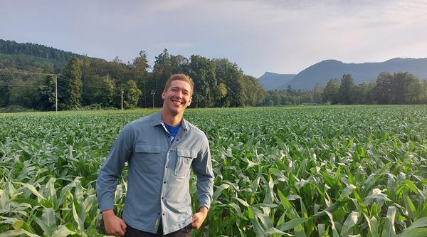 Douglas Groenendijk grins while standing in a vast green field with a mountain range behind him.