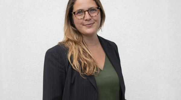 Dr. Amanda Wager, wearing a green shirt and black blazer, stands in front of a white wall.