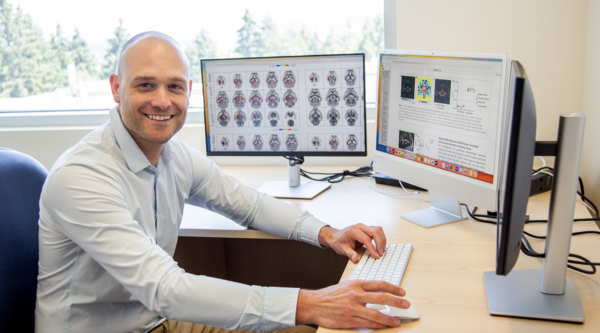 Dr. Sandy Shultz sitting at a desk in front of two computer screens and smiling at the camera.