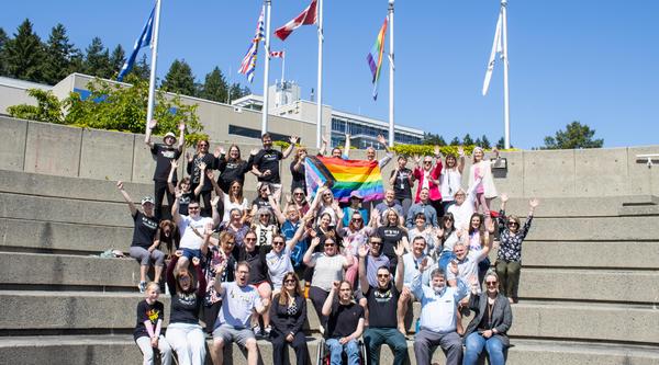 A group wearing Pride t-shirts poses for a photo with the pride flag