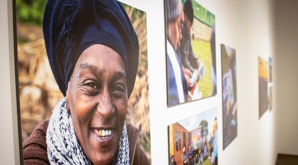 Four photographs hang on the gallery wall. The closest photo is of a person facing the camera smiling.