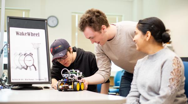 three students look at a robotic car on a table
