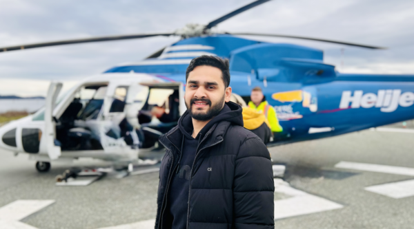 Saurya Mishra standing outside in front of a Heli-Jet helicopter and looking at the camera.