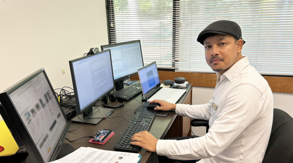 Dr. Ajay Shrestha sitting at his desk in front of multiple computer screens and looking at the camera.