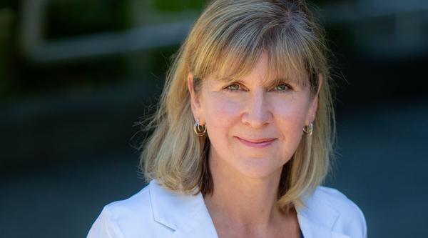 Kristie Dewald with a blurred background, wearing a white blazer