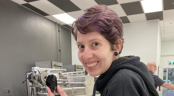 Melanie P. Loureiro stands in front of several bins of mussels and holds onel in her left hand.