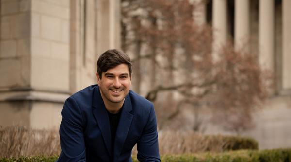 Michael MacKenzie sits on a bench in front of a stone building