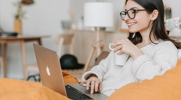 Woman smiles at her laptop screen, holding a cup of coffee