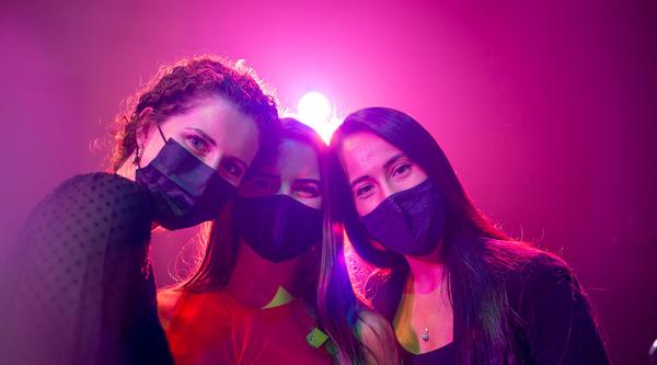 Three women posing in masks with a stage light behind them