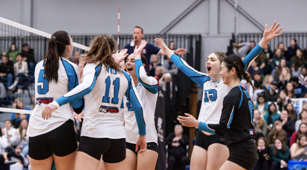 A group of VIU Mariners women's volleyball teammates celebrate in a circle on the volleyball court