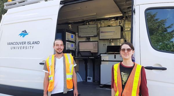 Trevor Michalchuk and Lily Eggert, wearing high visibility vests, while standing in front of the Mass Specmobile.
