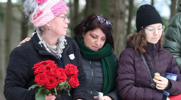 Eliza Gardiner holds a bouquet of red roses and stands next to Joy Gugeler and a student during the 2022 vigil.