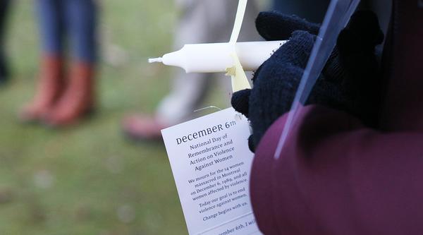 Someone holds a white candle with a tag that reads December 6th, National Day of Remembrance and Action on Violence Against Women
