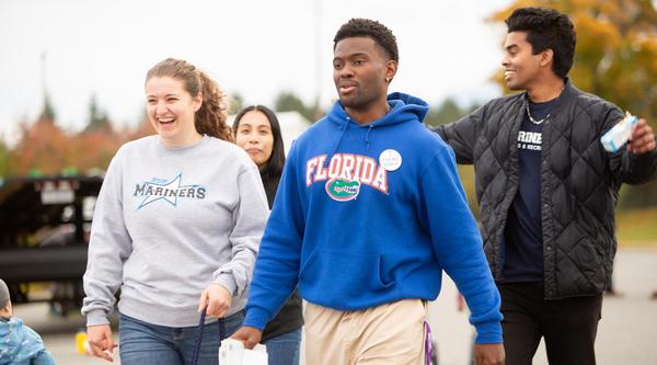Four students walk together with festival in background