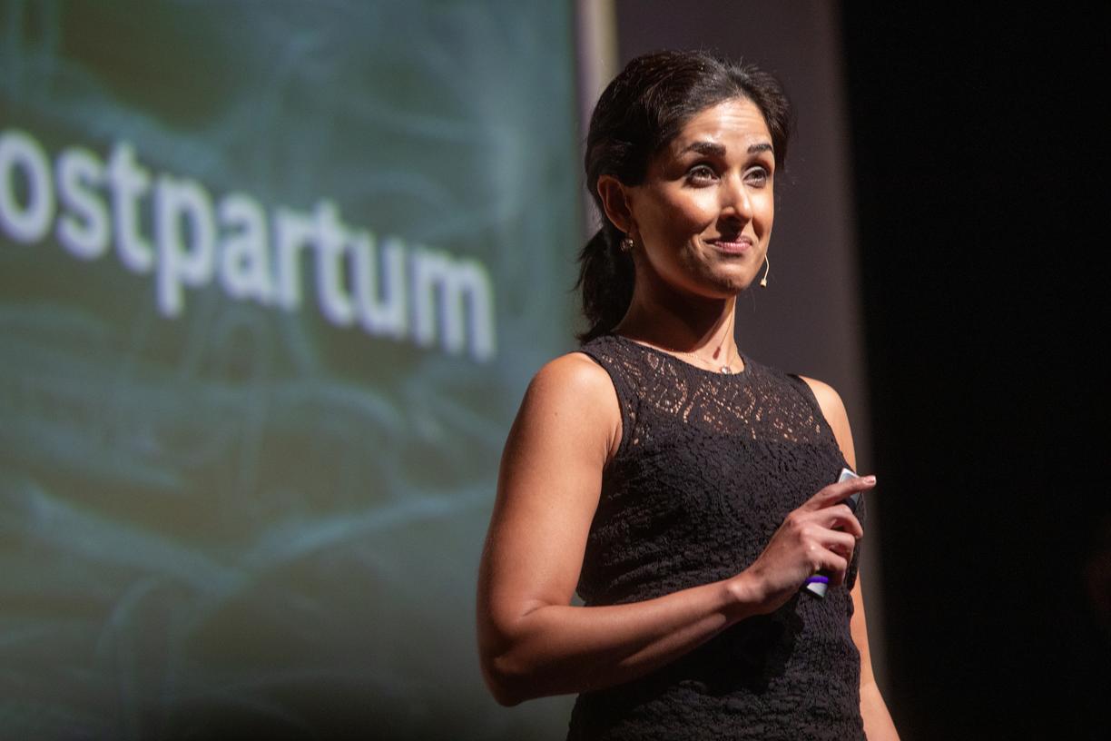 Dr. Shahana speaks on the stage with a clicker in her hand, wearing a mic set