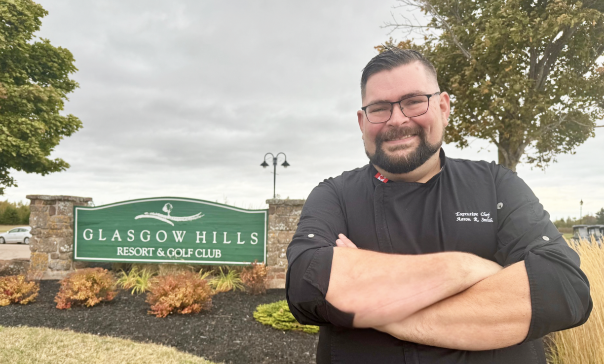 Aaron Smith standing by the Glasgow Hills resort sign with his arms folded and smiling at the camera.