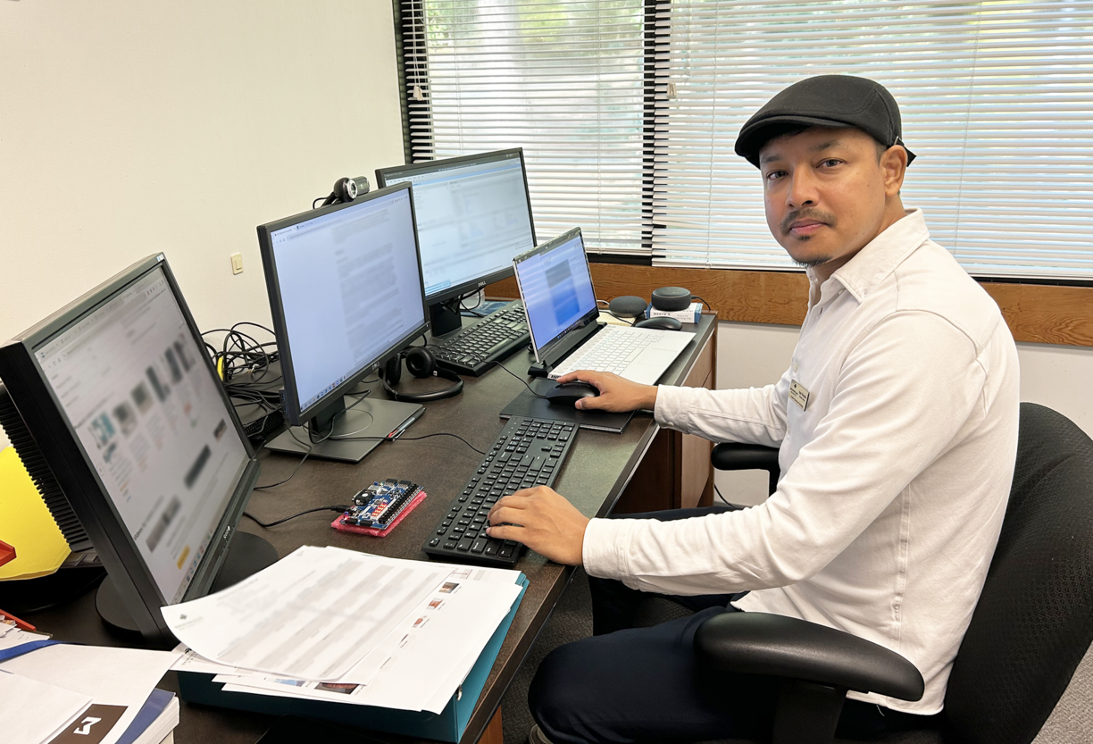 Dr. Ajay Shrestha sitting at his desk in front of multiple computer screens and looking at the camera.