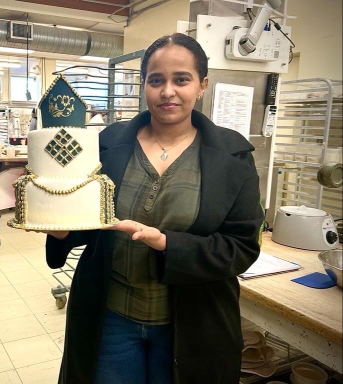 Zuhur Debasay holding a cake she made at VIU and smiling at the camera.