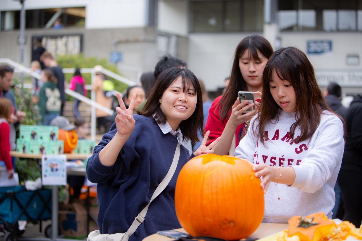 three students carve a pumpkin together