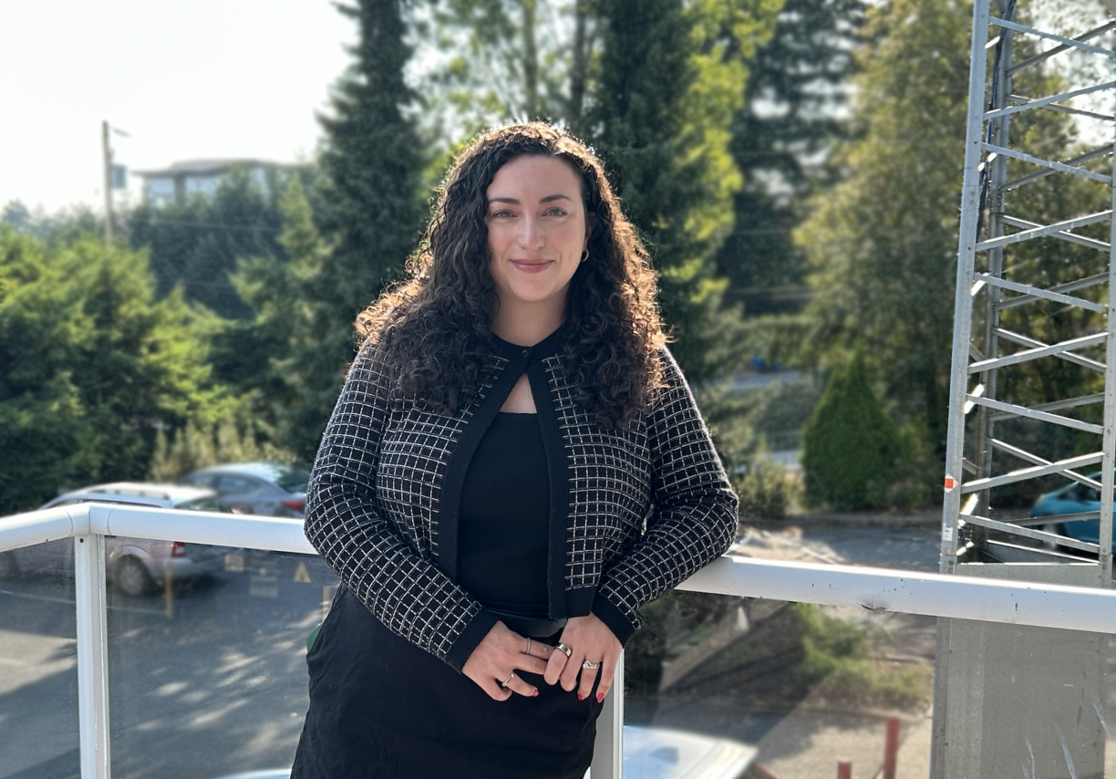 Caitlin Lundgren standing outside leaning on a railing on a sunny day and looking at the camera.