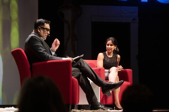 Two people sit on a stage in red chairs having a conversation