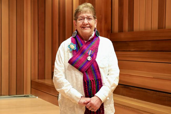 Métis Elder-in-Residence Stella Johnson standing in a cedar panelled room wearing a red and purple tartanMétis scarf with a King Charles III Coronation Medal