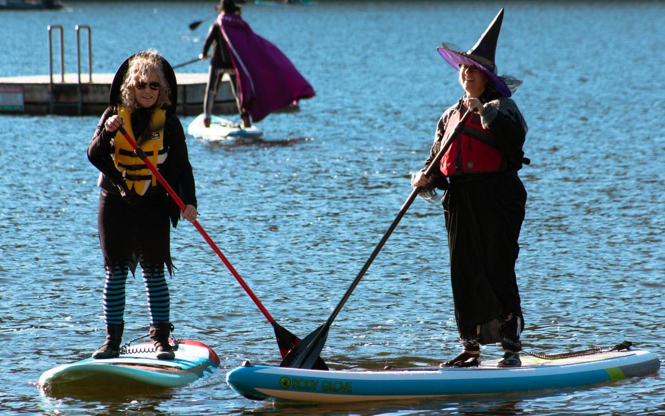 Two women dressed as witches paddle on Westwood Lake