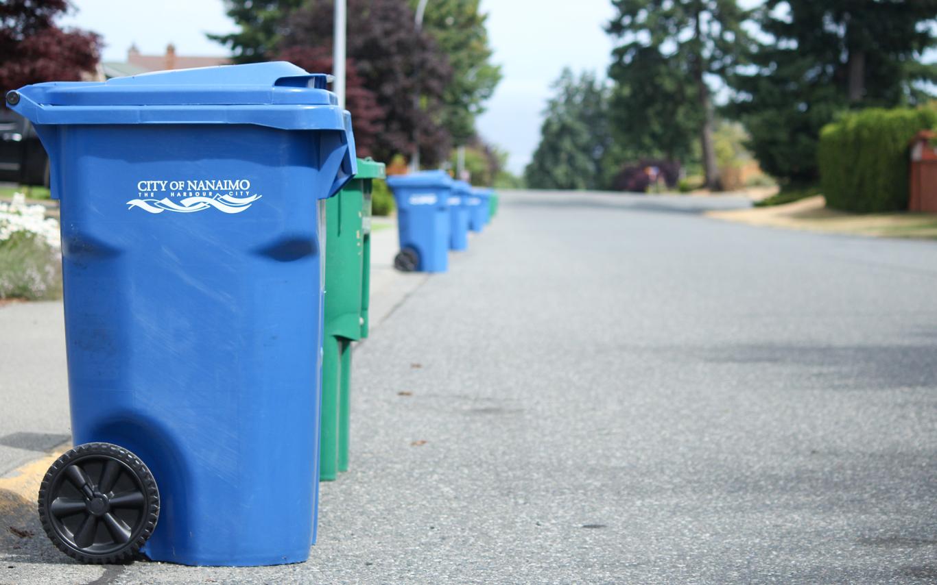 Blue garbage bins and green recycling bins line the left side of a Nanaimo street.