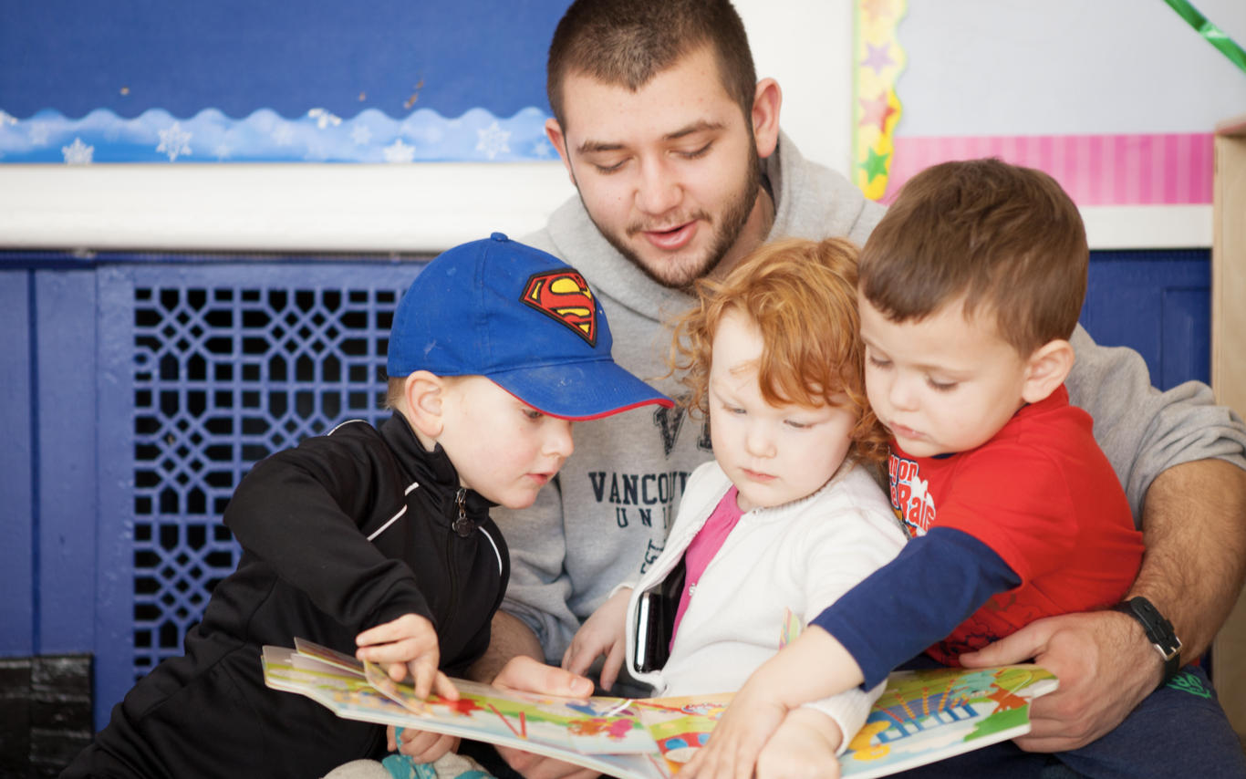 An early childhood educator reading a book to three kids