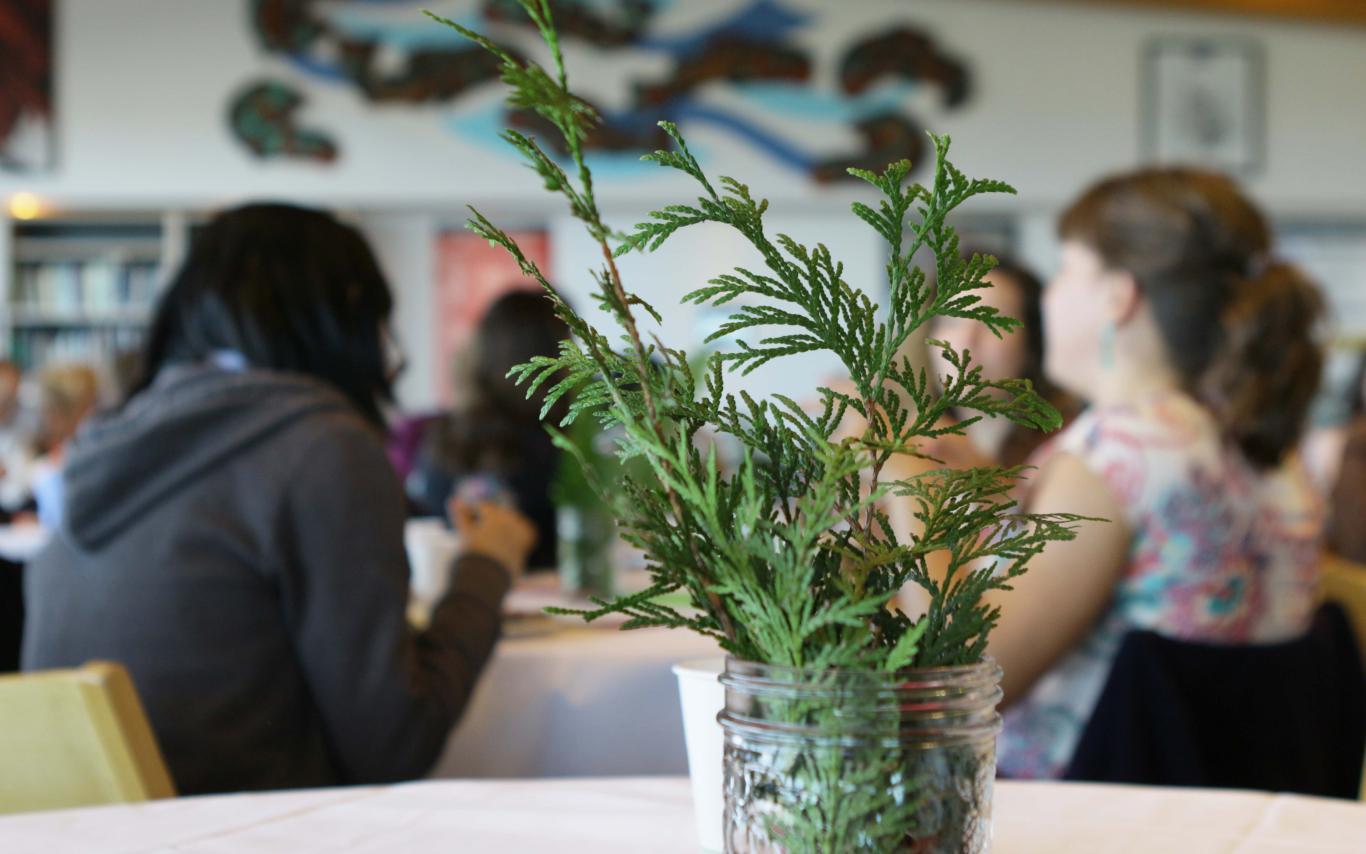 Cedar branch in a jar in foreground, people in VIU's Gathering Place in background