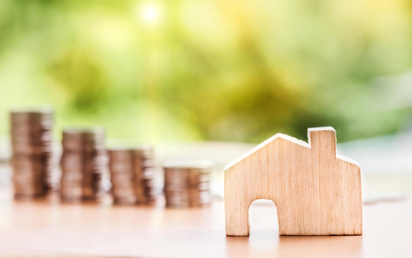A wooden cutout of a house with four stacks of coins behind it.