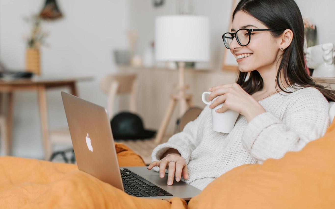 Woman smiles at her laptop screen, holding a cup of coffee