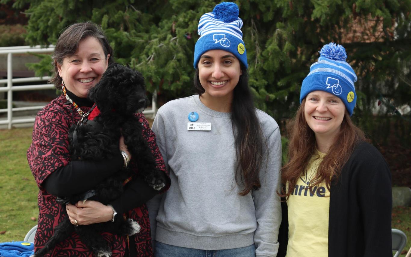 Three people pose, one of whom is holding a dog