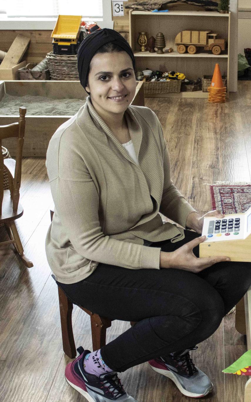Woman sits in the middle of a preschool room. 